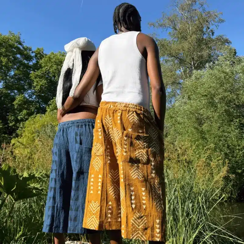 Shorts baggy en bogolan bleu et ocre portés de dos par un couple, mode africaine en extérieur