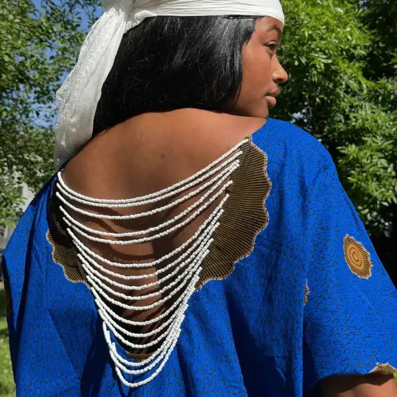 Robe Àkua en wax bleu vue de dos, dos ouvert orné de perles blanches, portée en extérieur