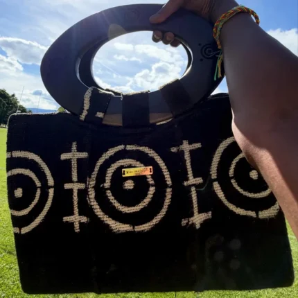 Sac à main Aabò en bogolan noir tenu à la main, motifs beiges et anse ronde en bois