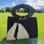 Sac à main noir et blanc avec un design abstrait, équipé d'une poignée supérieure ovale en bois sombre et de détails décoratifs circulaires.