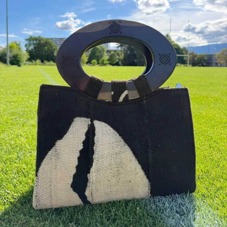 Sac à main noir et blanc avec un design abstrait, équipé d'une poignée supérieure ovale en bois sombre et de détails décoratifs circulaires.