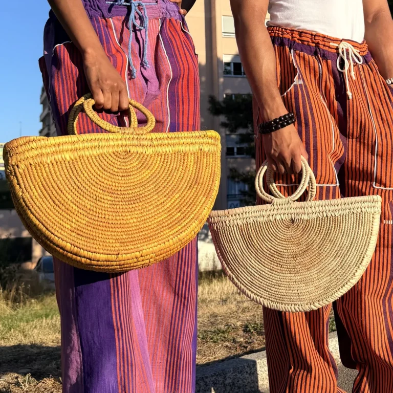 Deux paniers demi-lune en raphia tressé, un jaune et un naturel, à anses rondes, portés à la main